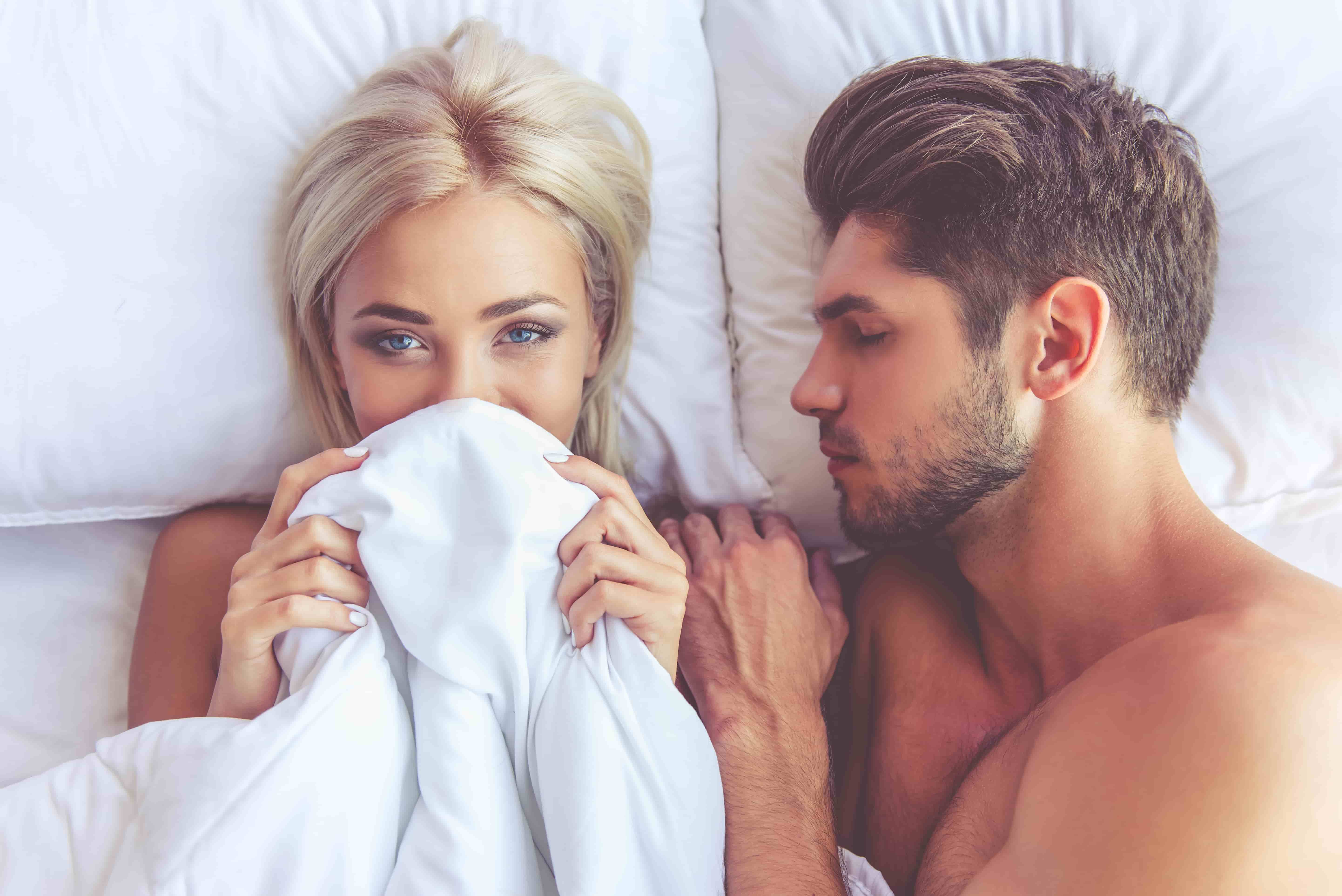 couple in bed woman covering face with blanket